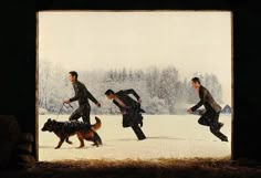 three men are running in the snow with their dogs