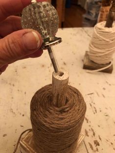 a person holding a ball of string and a spool of twine on top of a table