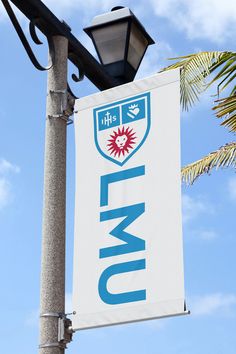 a sign hanging off the side of a light pole next to a palm tree and blue sky