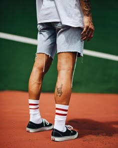 a man with tattoos on his legs standing on a tennis court holding a racquet