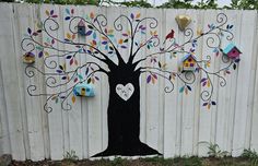 a tree painted on the side of a fence with birdhouses and hearts attached to it