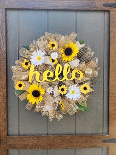 a wreath with sunflowers and the word hello is hanging on a wooden door