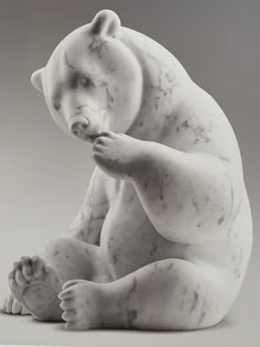 a white statue of a bear sitting on its hind legs and looking at the ground