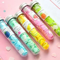 four different colored pens sitting next to each other on a pink surface with confetti sprinkles