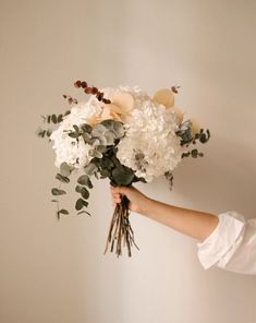 a woman holding a bouquet of white and grey flowers in her hand with greenery