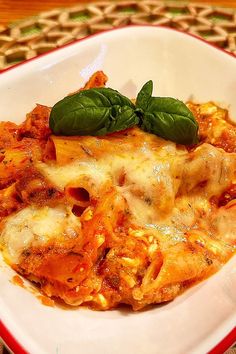 a white plate topped with lasagna covered in sauce and cheese, garnished with basil