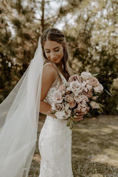 a woman in a wedding dress is holding a bouquet and looking down at her veil