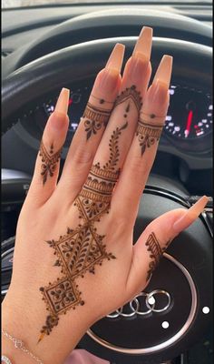 a woman's hand with henna tattoos on her left wrist and the steering wheel behind her