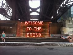 two women are sitting on the ground in front of a sign that reads welcome to the bronx