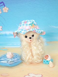 a small white dog sitting on top of a sandy beach next to a blue hat