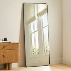 a large mirror sitting on top of a wooden table next to a dresser and window