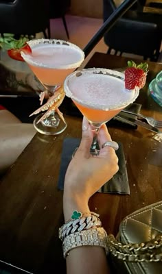 two people holding up martinis with strawberries on the rim and one person's hand