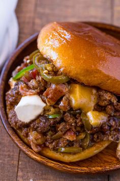 a sloppy joe sandwich with cheese and peppers on a wooden plate, ready to be eaten