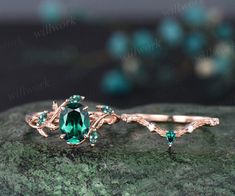 a close up of a ring on a rock with green stones and leaves around it