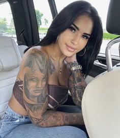 a woman sitting in the back seat of a car with tattoos on her arm and shoulder