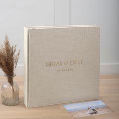 a wedding album sitting on top of a table next to a vase filled with dried flowers