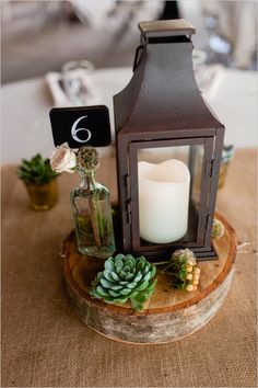 a candle and some succulents are sitting on a wood slice with a table number