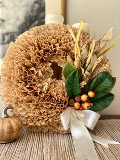 a wreath with leaves, berries and other decorations sits on a table next to a pumpkin