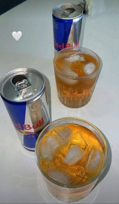 three cans and two glasses filled with drinks on a white counter top next to each other