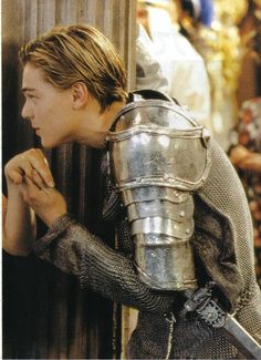 the young man is dressed in armor and holding his hand up to his face as he leans against a wall