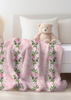 a teddy bear sitting on top of a bed next to a pink flowered blanket