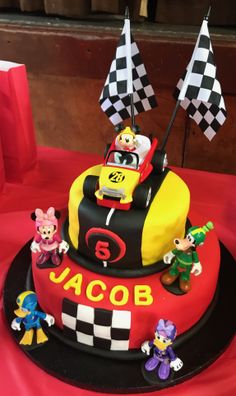 a birthday cake with mickey mouse and other characters on the top is sitting on a red tablecloth