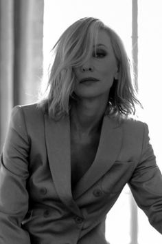 black and white photograph of a woman in a suit sitting on a chair with her hands behind her back