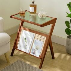 a small table with magazines on it next to a white chair and potted plant