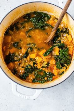 a pot full of soup with spinach and carrots on the side next to a wooden spoon