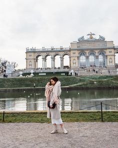 a woman standing in front of a building with a lake and fountain behind her,