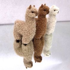 four stuffed llamas are hanging upside down on a white surface, with one alpaca in the foreground