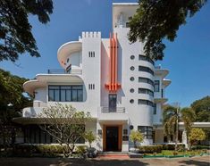 a large white building with an orange sculpture on it's side and trees in front