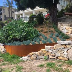 a large metal planter sitting on top of a lush green hillside next to a stone wall