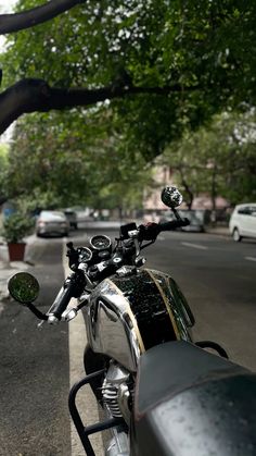 a motorcycle parked on the side of a road next to a tree and sidewalk with cars