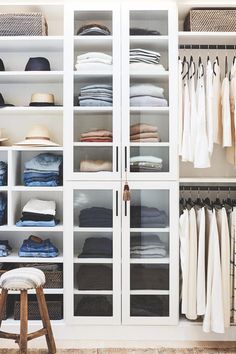 a white closet filled with lots of clothes and hats on top of glass shelves next to a stool