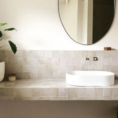 a white sink sitting under a round mirror next to a vase with a plant in it