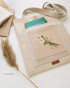 a bag with flowers on it sitting next to an open book and some dried grass