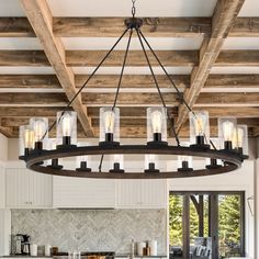 a large chandelier hanging from the ceiling in a kitchen with white cabinets and wooden beams