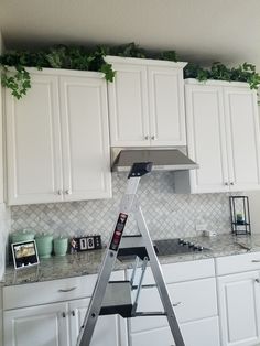 a kitchen with white cabinets and a ladder in front of the counter top that has plants growing on it