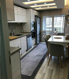 an open kitchen and dining room area with white cabinets, grey rugs and light wood flooring