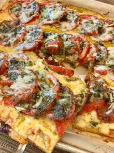 a pizza with tomatoes and spinach on it is cut into four slices, sitting on a wooden table