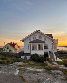 a white house sitting on top of a lush green field next to the ocean at sunset