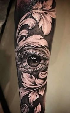 an eye tattoo on the arm with flowers and leaves around it, in black and white