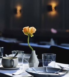 an orange flower in a vase on a table with empty plates and cups around it