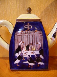 a ceramic teapot with ducks and geese in a cage on the front, sitting on a table