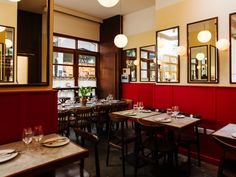 an empty restaurant with red walls and wooden tables set for two people to sit at