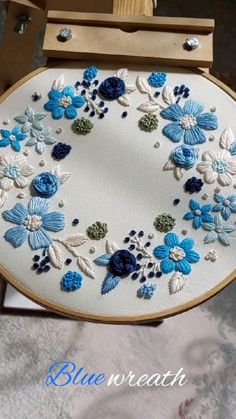 an embroidered blue and white flower design on a wooden frame