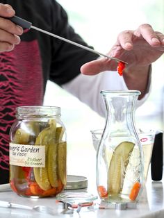 two people are preparing pickles in glass jars