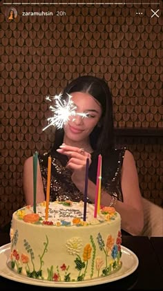 a woman holding a sparkler in front of a cake with lit candles on it