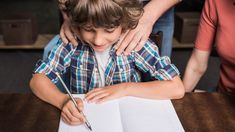 a young boy sitting at a table with an open book in front of him and his mother